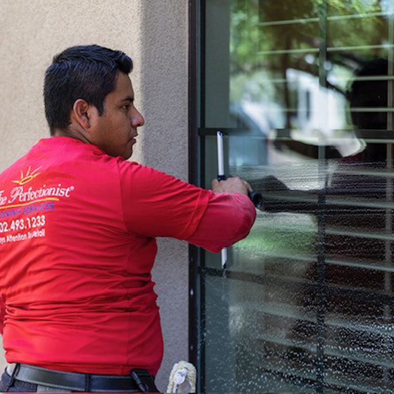 A man in a red shirt cleans a window, showcasing professional apartment washing services in Phoenix.