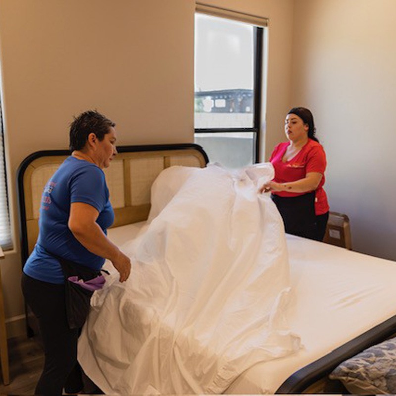 Two women are arranging a sheet on a bed, showcasing bedroom cleaning services in Phoenix, AZ.