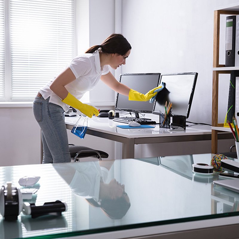 A woman wearing rubber gloves cleans a monitor, showcasing office cleaning services in Phoenix, AZ.