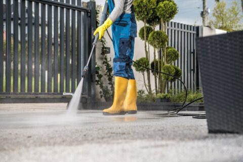 A worker in boots & overalls cleans a driveway in Phoenix, AZ, showcasing summer cleaning services.