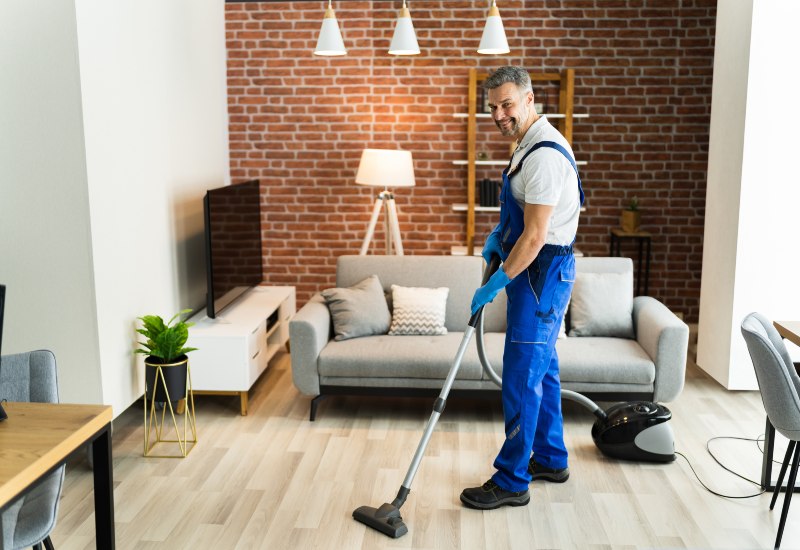 A Man in uniform vacuuming a living room, showcasing professional floor cleaning in Phoenix, AZ.