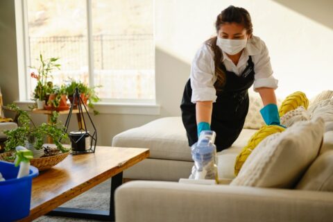 A woman in a mask cleans a living room, representing maid vs. housekeeping services in Phoenix, AZ