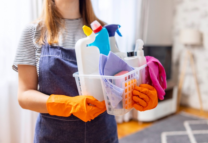 Woman in rubber gloves with basket of cleaning supplies, ready to clean up in Phoenix, AZ