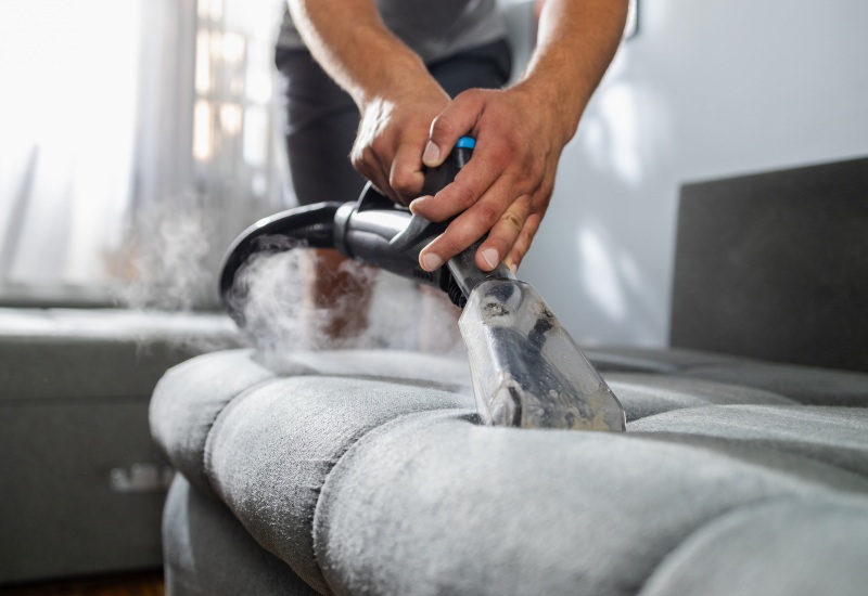 A man performing deep steam cleaning on the sofa upholstery in Phoenix, AZ