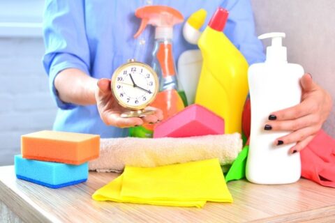 Cleaning supplies, sponges, cloths, and a clock arranged on a table