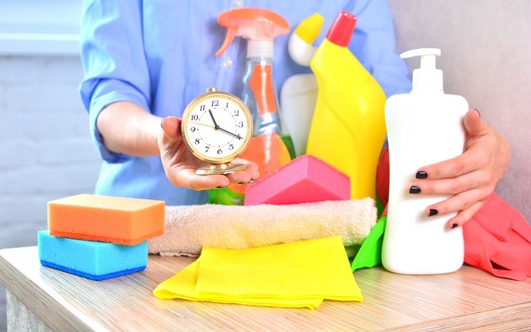Cleaning supplies, sponges, cloths, and a clock arranged on a table