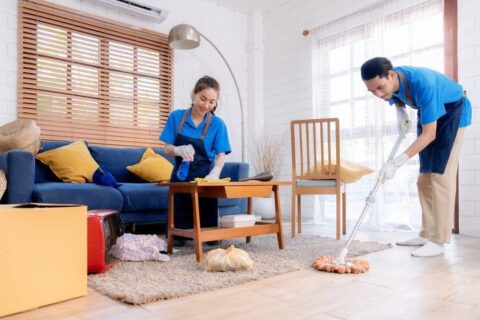 Two professional cleaners mopping and wiping surfaces in a living room