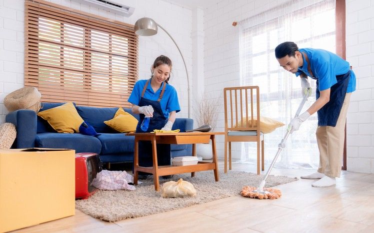 Two professional cleaners mopping and wiping surfaces in a living room