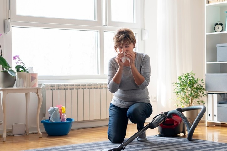 A woman vacuuming a rug at home with cleaning supplies nearby